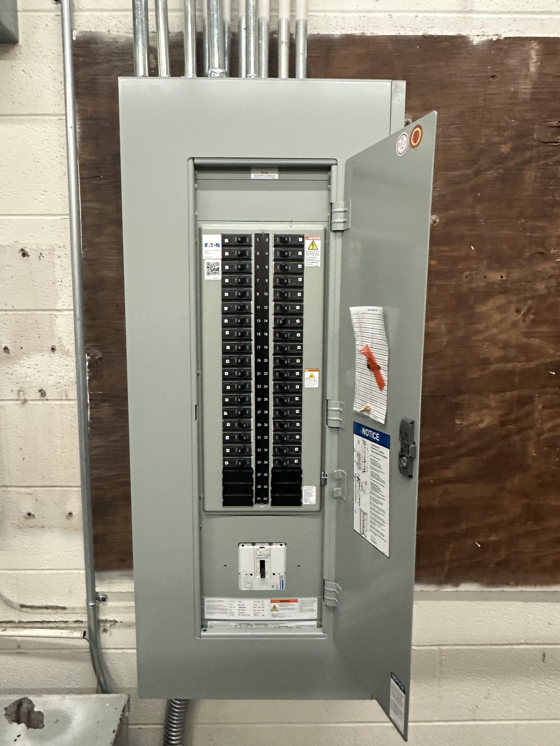 An open electrical breaker panel with multiple circuit breakers and labels on the inside of the door, mounted on a wall.